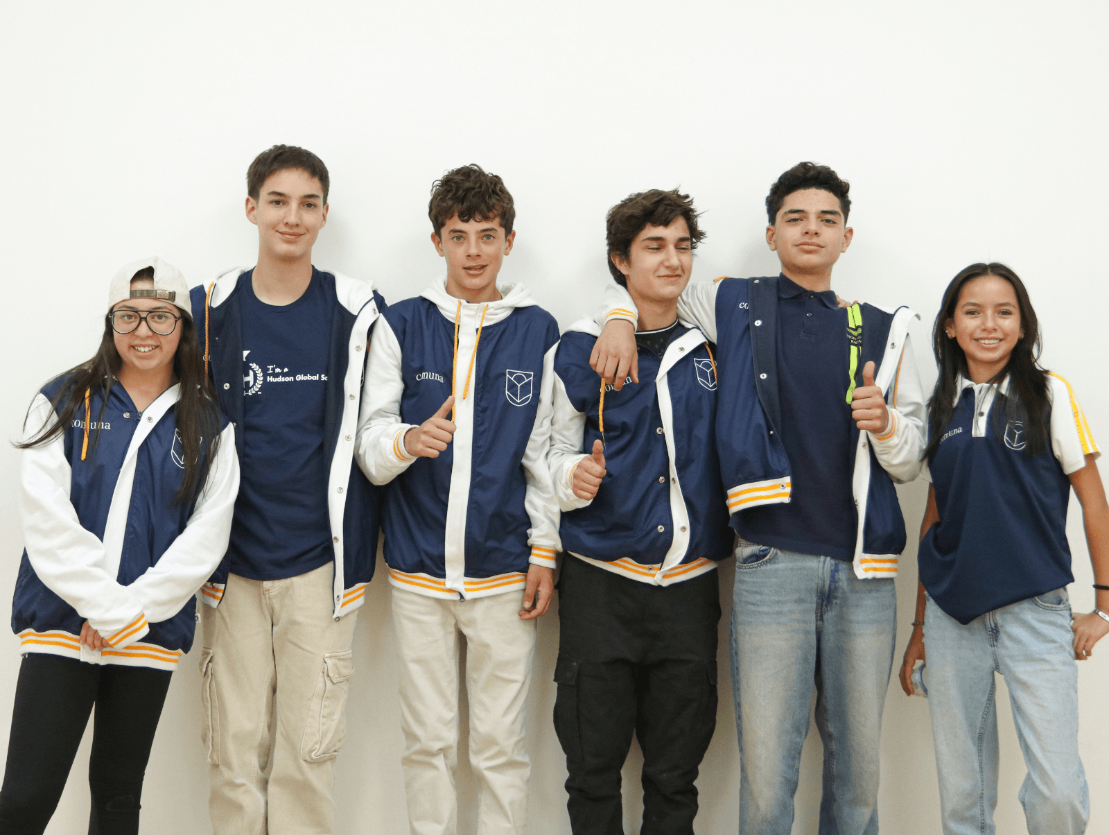 Seis estudiantes de Comuna con sus chaquetas institucionales posando junto a una pared blanca