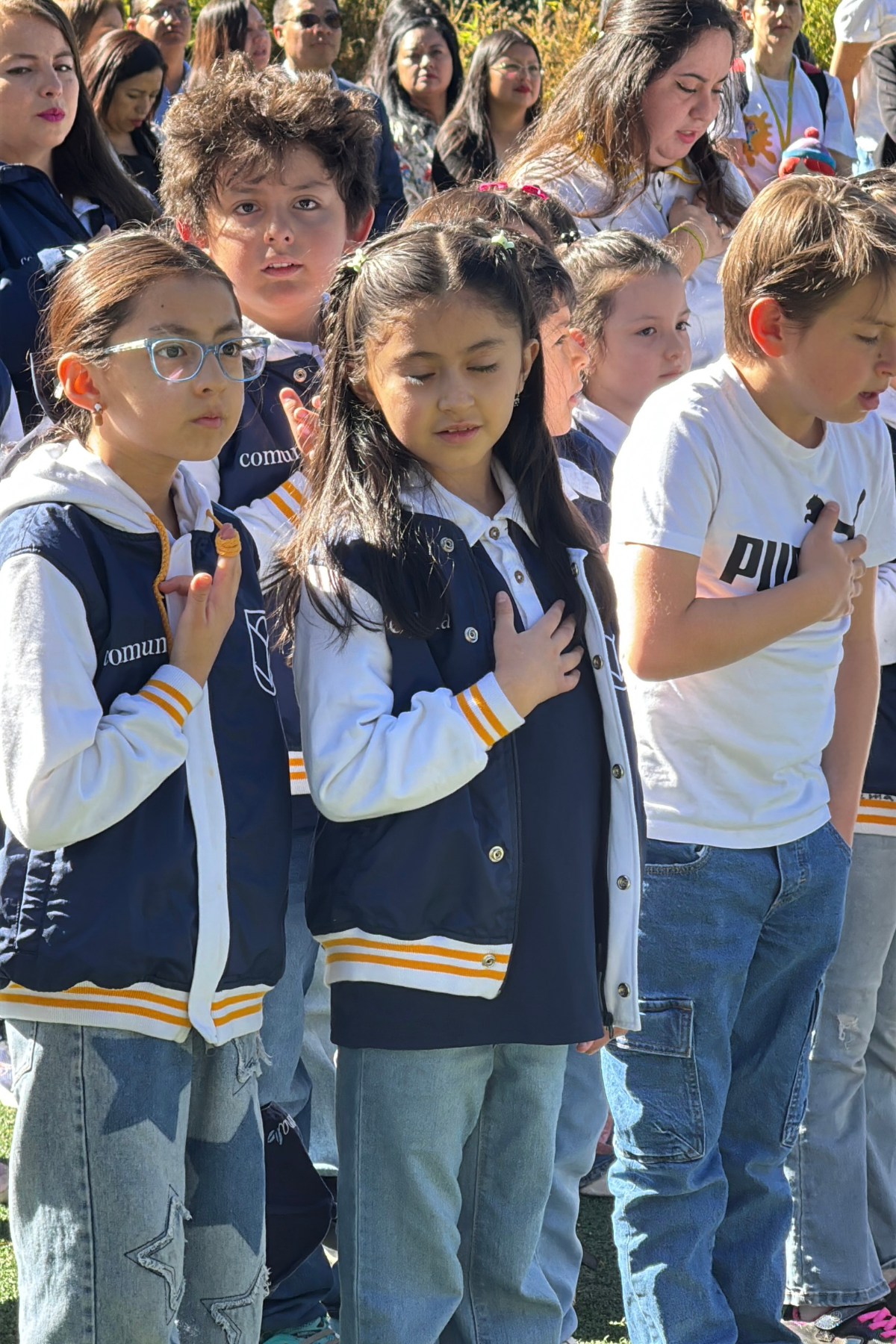 Niñas y niños de Comuna con la mano en el pecho durante un acto cívico