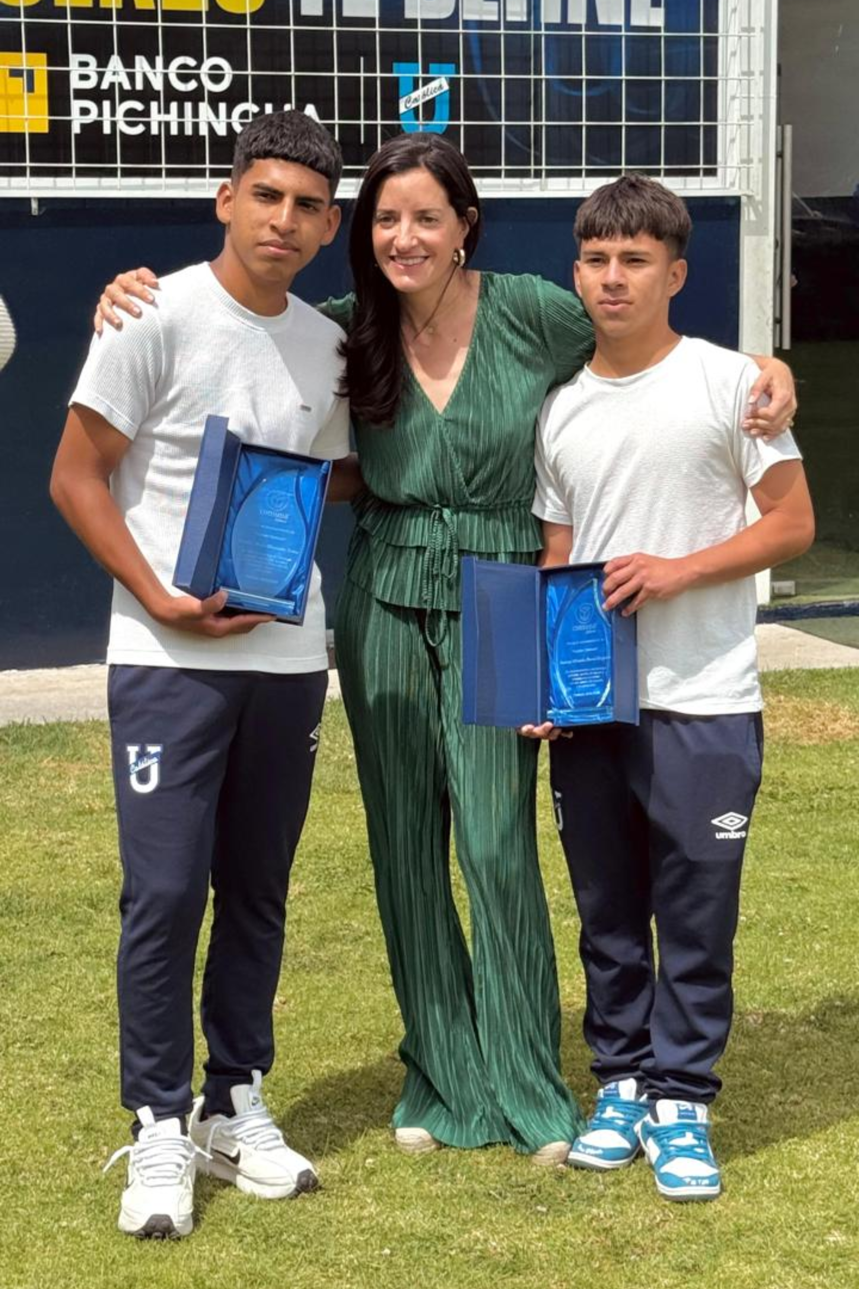 Integrante de Fundación Comuna junto a dos jóvenes atletas que reciben reconocimientos en la cancha de la Universidad Católica