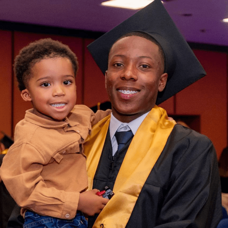 Graduado con toga cargando a un niño pequeño